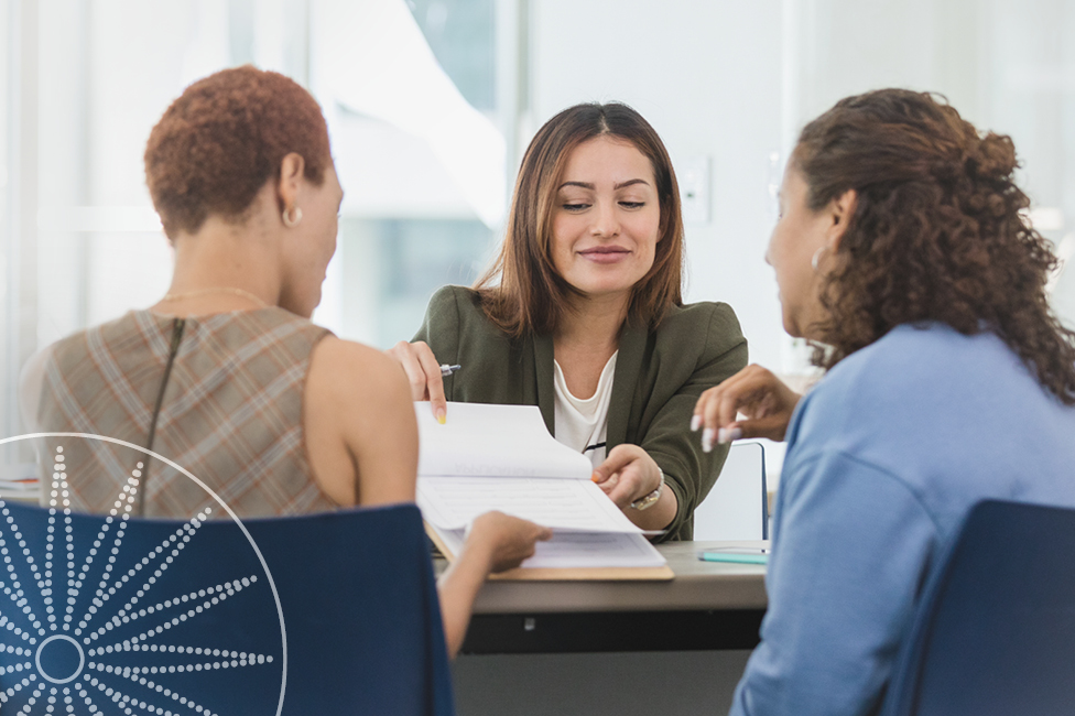 A female advisor speaking to two female clients at an office desk